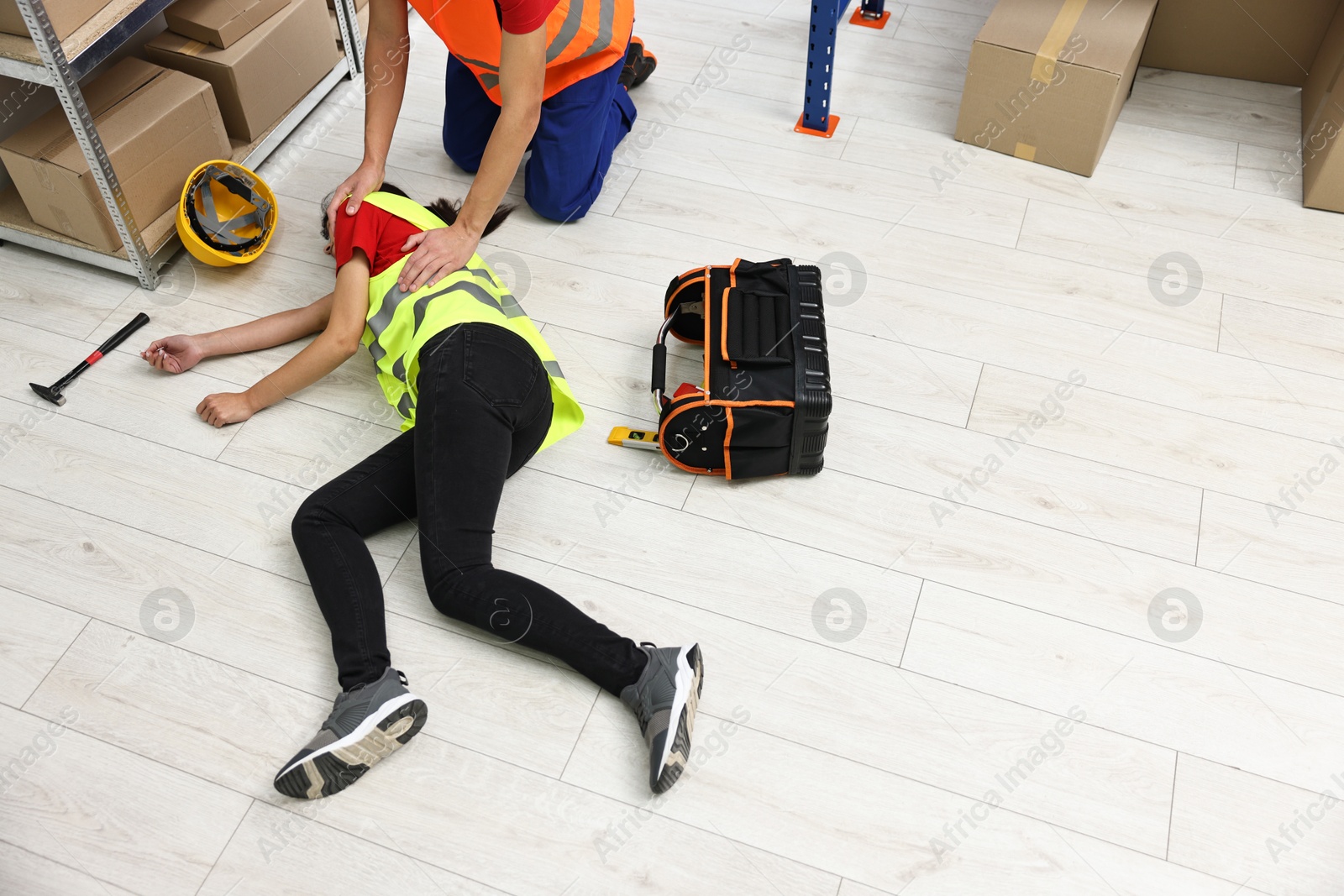 Photo of Accident at work. Man helping his unconscious colleague in warehouse. Space for text