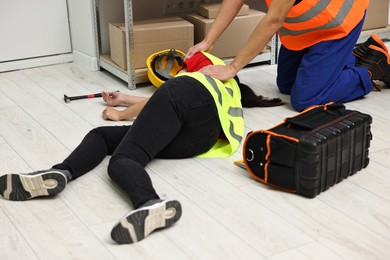 Photo of Accident at work. Man helping his unconscious colleague in warehouse