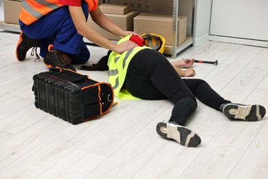 Photo of Accident at work. Man helping his unconscious colleague in warehouse