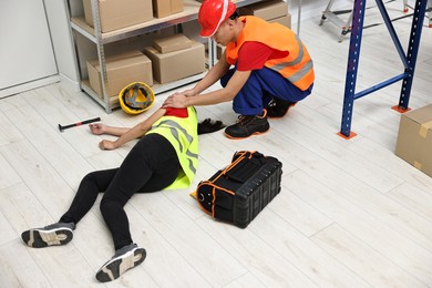 Photo of Accident at work. Man helping his unconscious colleague in warehouse