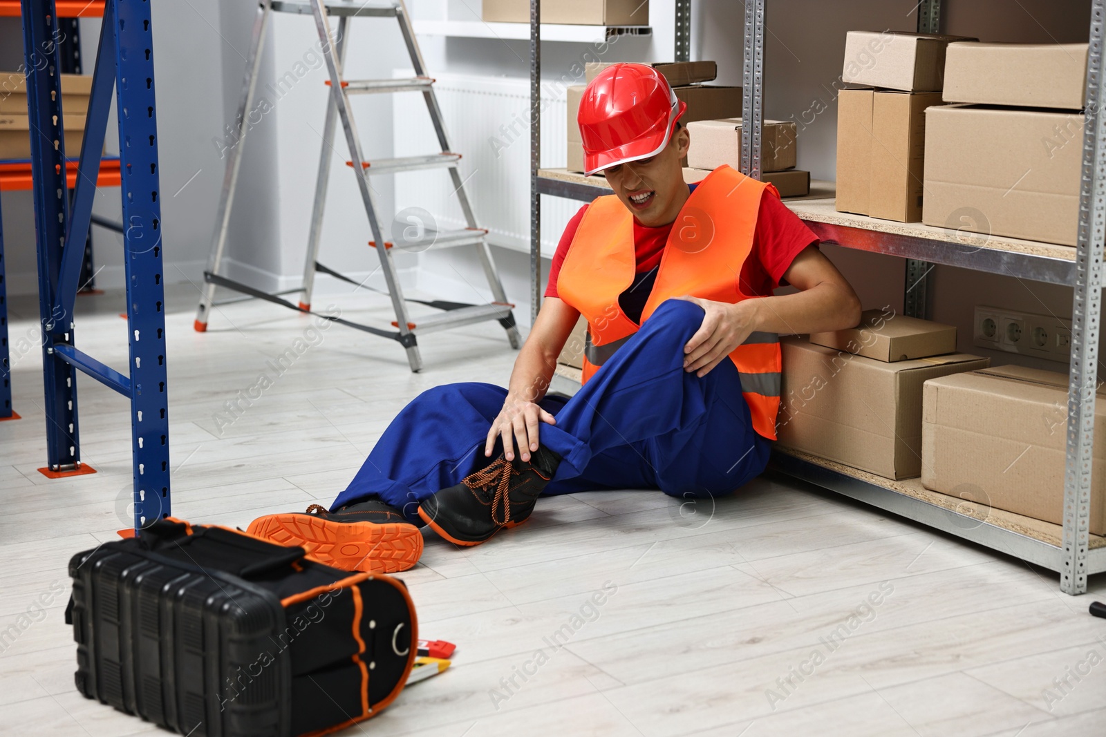 Photo of Accident at work. Injured man with toolkit on floor in warehouse