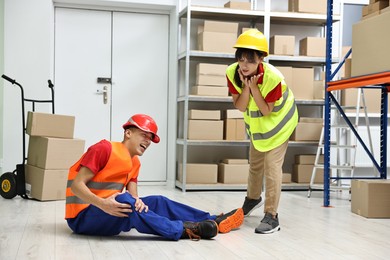 Photo of Accident at work. Woman helping her injured colleague in warehouse