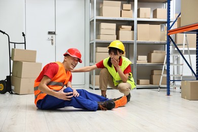 Photo of Accident at work. Woman helping her injured colleague in warehouse