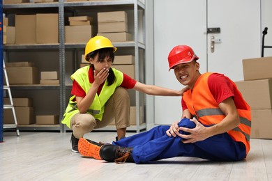 Photo of Accident at work. Woman helping her injured colleague in warehouse