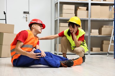 Photo of Accident at work. Woman helping her injured colleague in warehouse