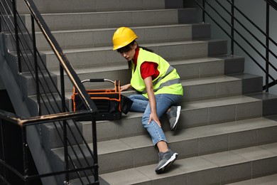 Photo of Accident at work. Injured woman with toolkit on stairs indoors