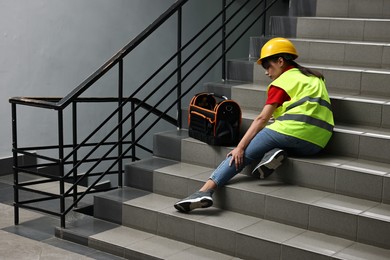 Photo of Accident at work. Injured woman with toolkit on stairs indoors. Space for text