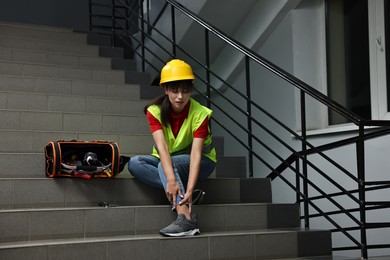 Photo of Accident at work. Injured woman with toolkit on stairs indoors