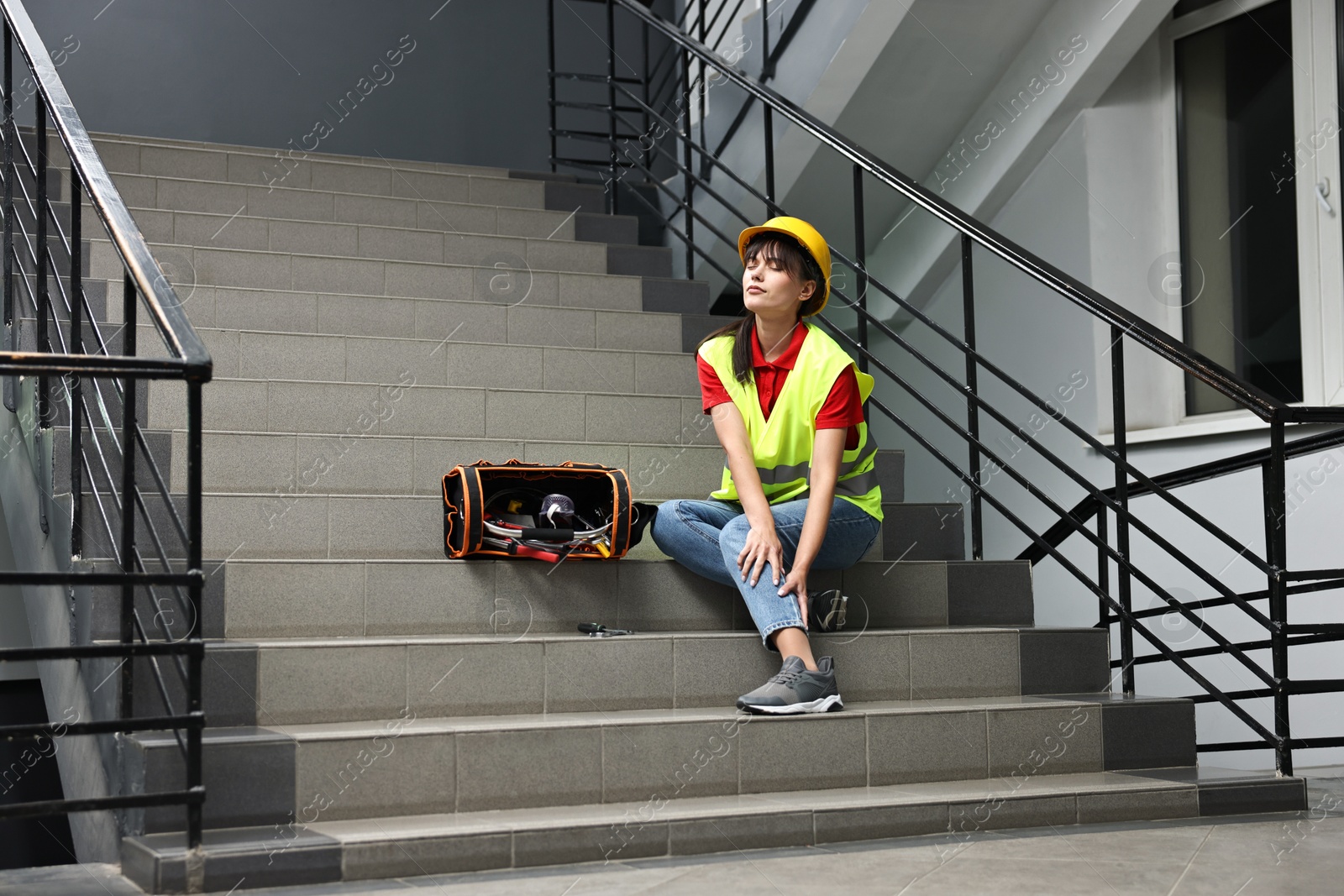 Photo of Accident at work. Injured woman with toolkit on stairs indoors