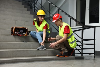 Photo of Accident at work. Man helping his injured colleague on stairs indoors