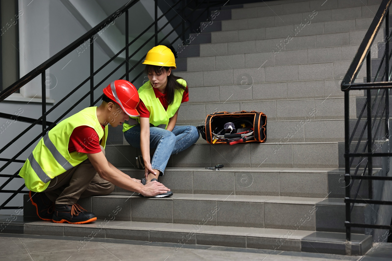 Photo of Accident at work. Man helping his injured colleague on stairs indoors