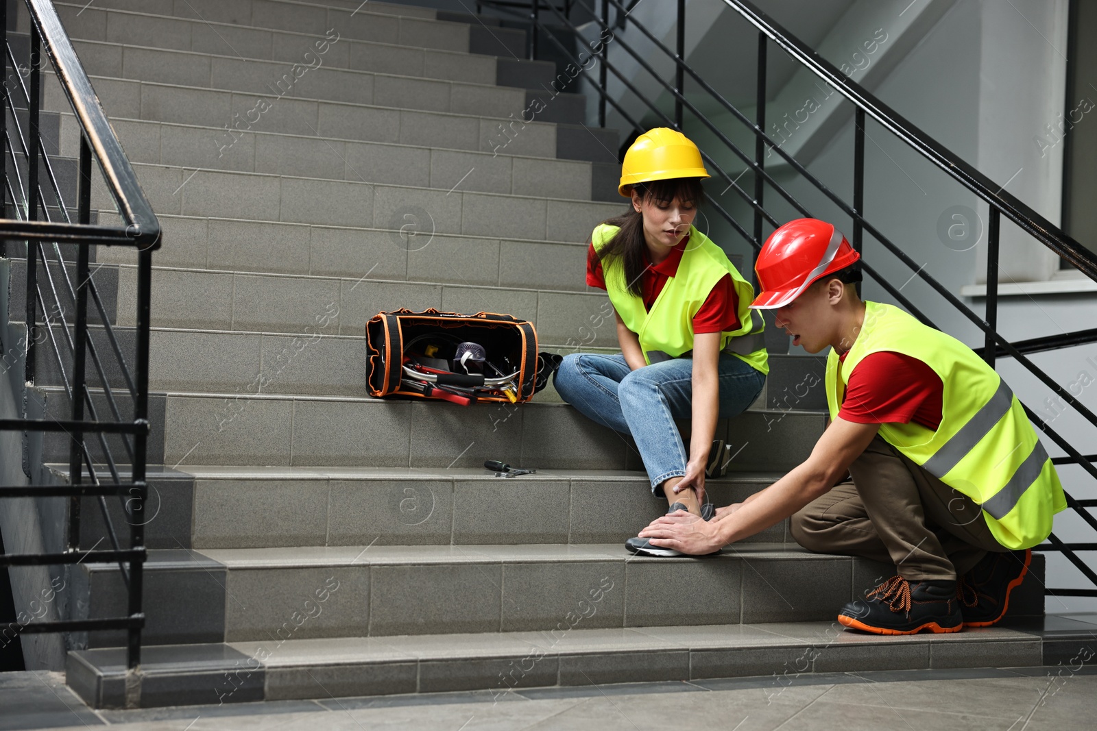 Photo of Accident at work. Man helping his injured colleague on stairs indoors