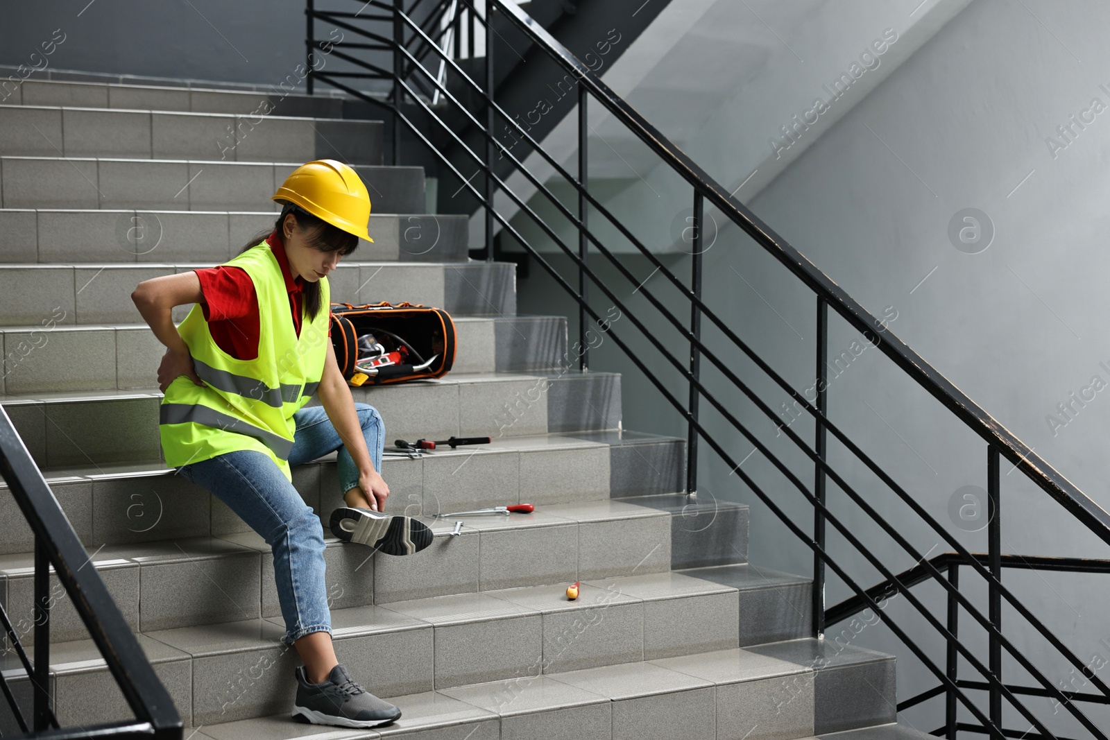 Photo of Accident at work. Injured woman with toolkit on stairs indoors. Space for text