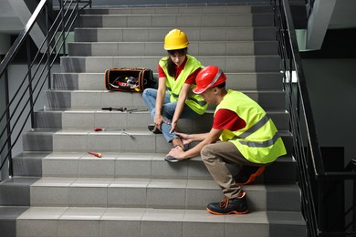 Photo of Accident at work. Man helping his injured colleague on stairs indoors