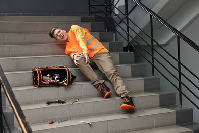 Photo of Accident at work. Injured man with toolkit on stairs indoors