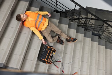 Accident at work. Unconscious man with toolkit on stairs indoors, above view