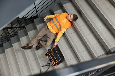 Photo of Accident at work. Unconscious man with toolkit on stairs indoors, above view