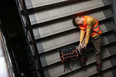 Photo of Accident at work. Injured man with toolkit on stairs indoors, above view. Space for text