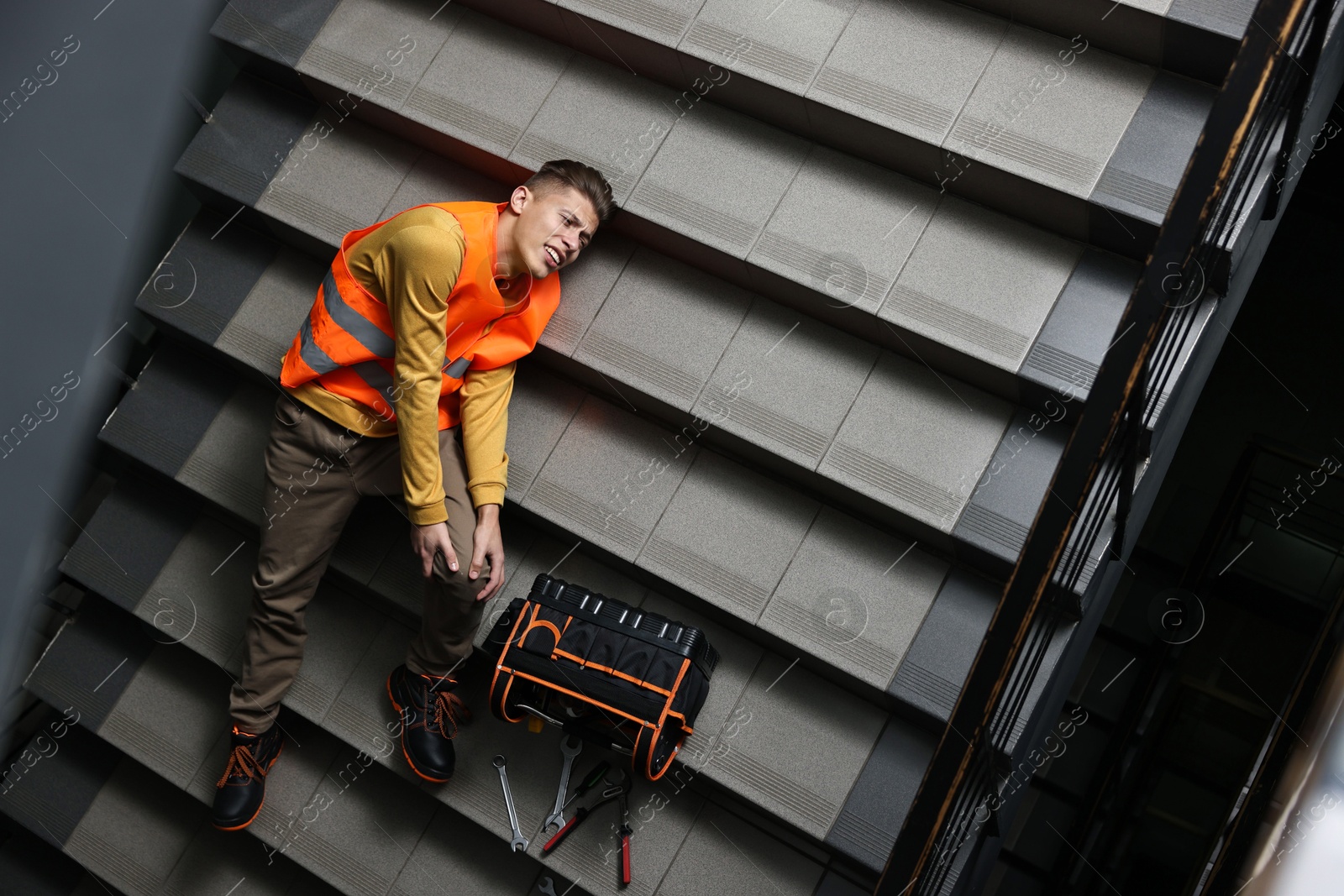 Photo of Accident at work. Injured man with toolkit on stairs indoors, above view. Space for text