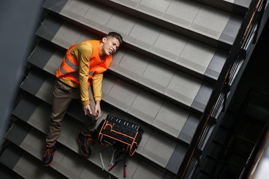 Photo of Accident at work. Injured man with toolkit on stairs indoors, above view. Space for text