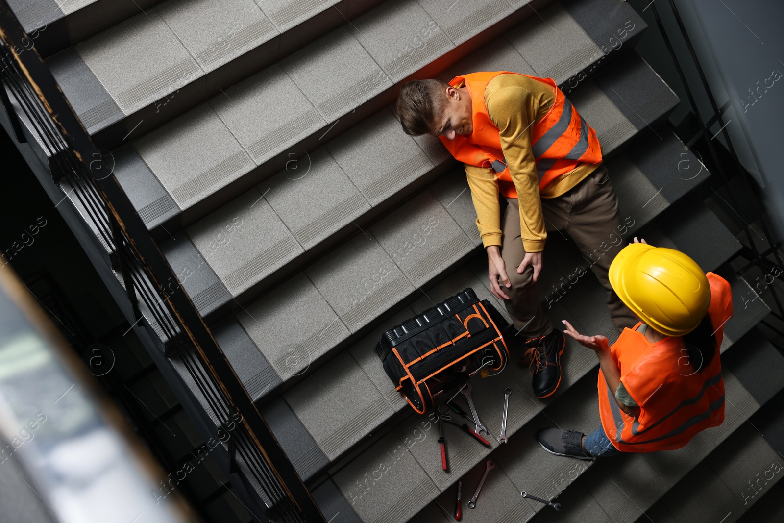 Photo of Accident at work. Woman helping her injured colleague on stairs indoors, above view. Space for text