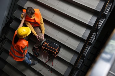 Photo of Accident at work. Woman helping her injured colleague on stairs indoors, above view. Space for text