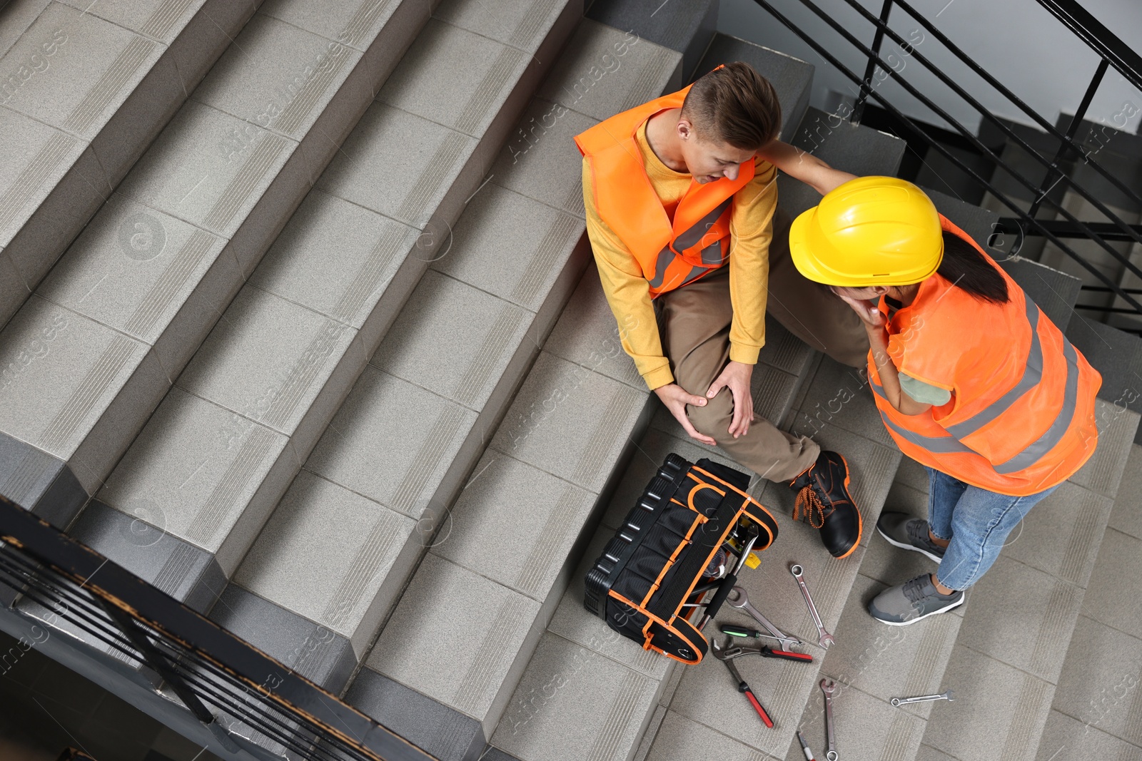 Photo of Accident at work. Woman helping her injured colleague on stairs indoors, above view. Space for text