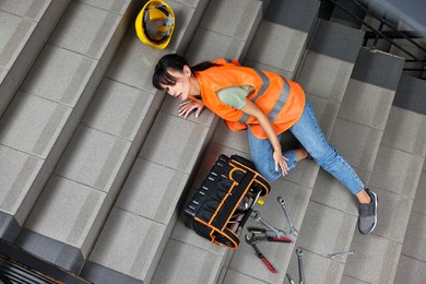 Photo of Accident at work. Injured woman with toolkit on stairs indoors, above view