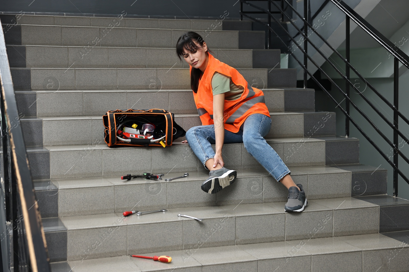 Photo of Accident at work. Injured woman with toolkit on stairs indoors