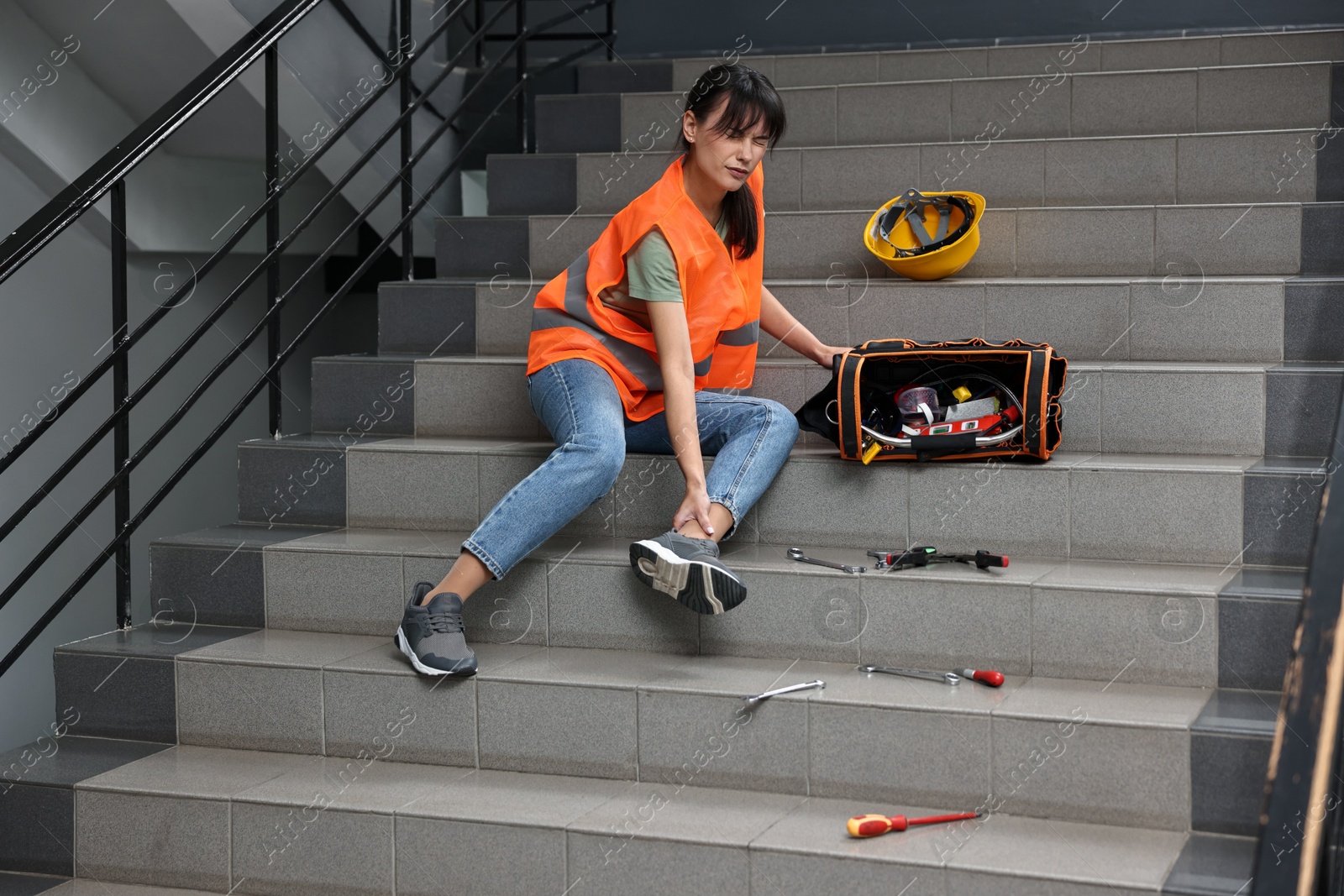 Photo of Accident at work. Injured woman with toolkit on stairs indoors