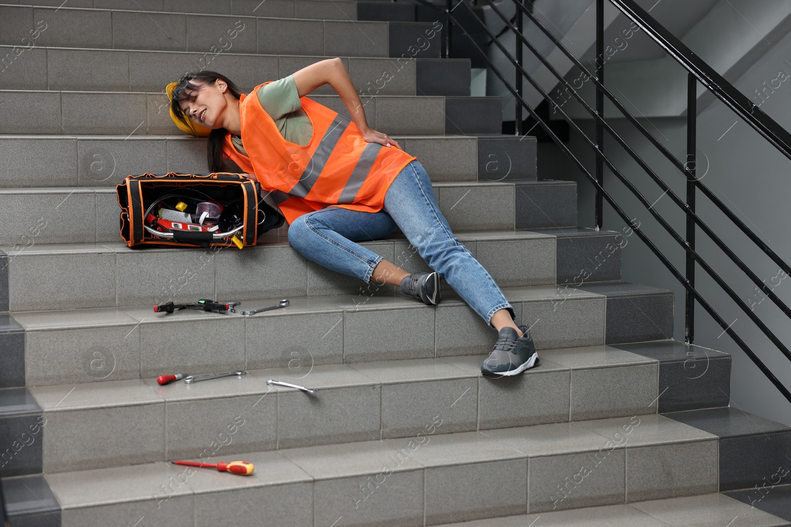 Photo of Accident at work. Injured woman with toolkit on stairs indoors