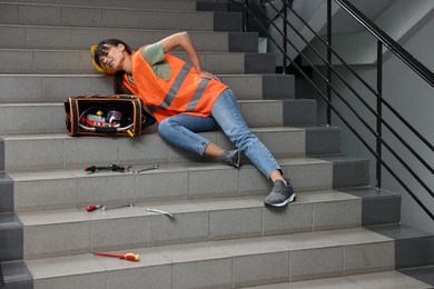 Photo of Accident at work. Injured woman with toolkit on stairs indoors