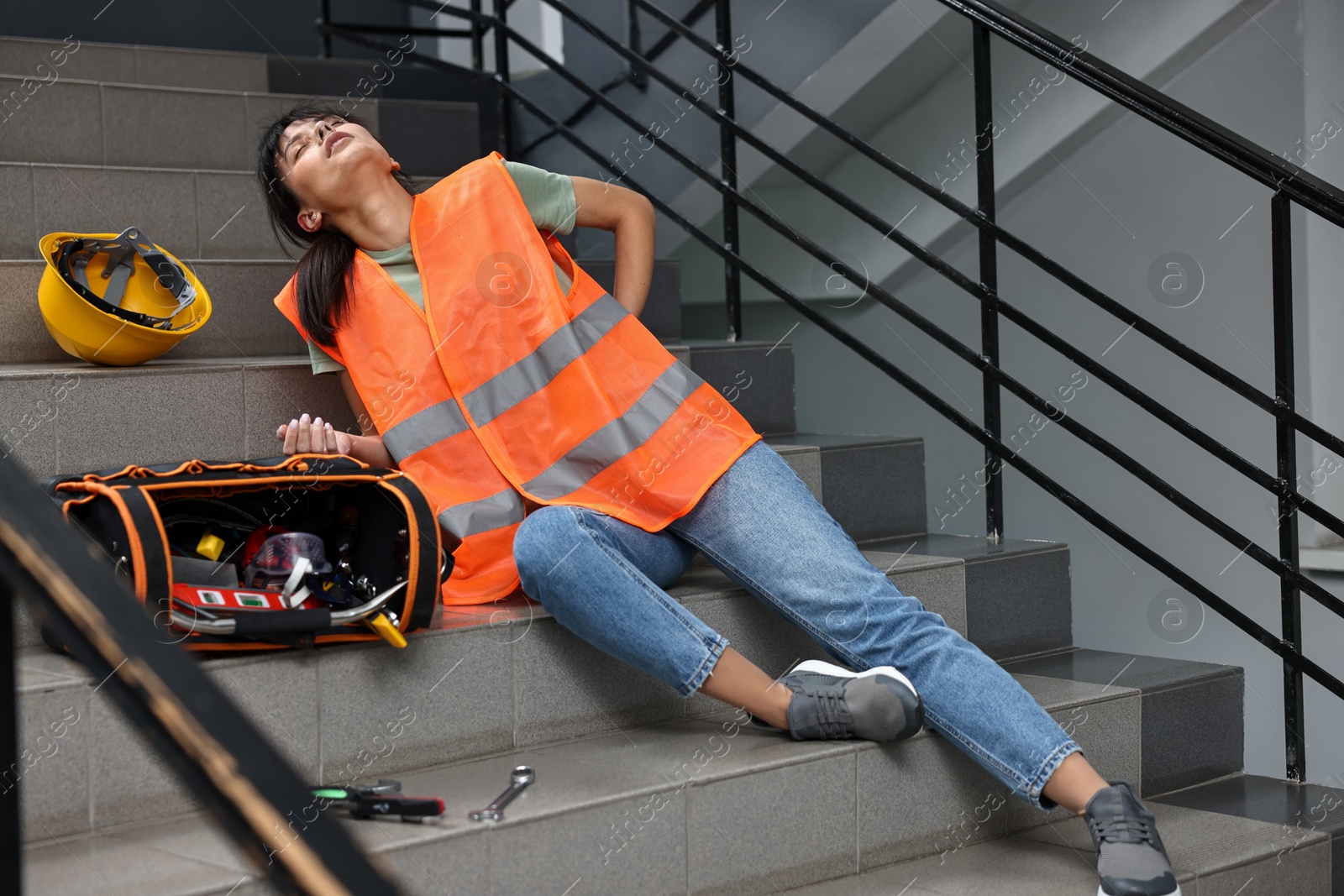 Photo of Accident at work. Injured woman with toolkit on stairs indoors