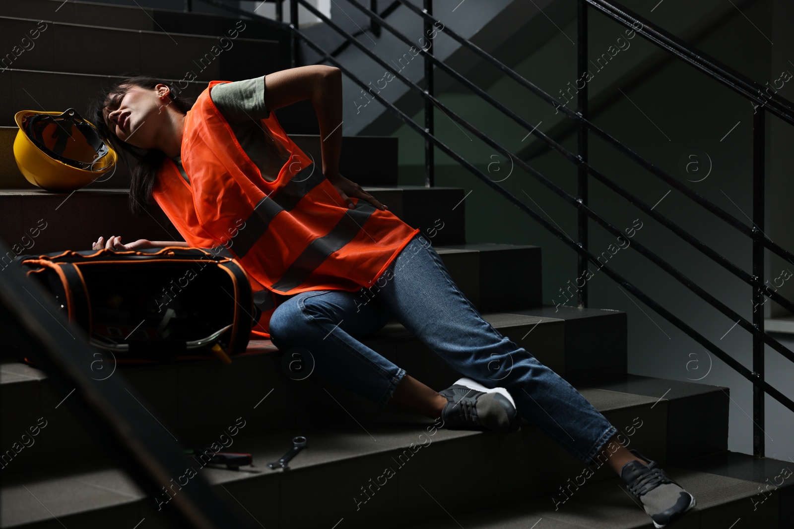 Photo of Accident at work. Injured woman with toolkit on stairs indoors