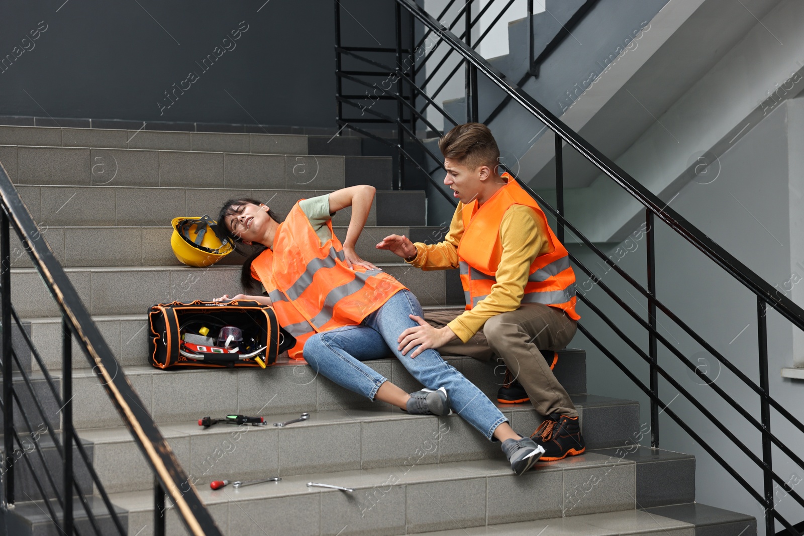 Photo of Accident at work. Man helping his injured colleague on stairs indoors