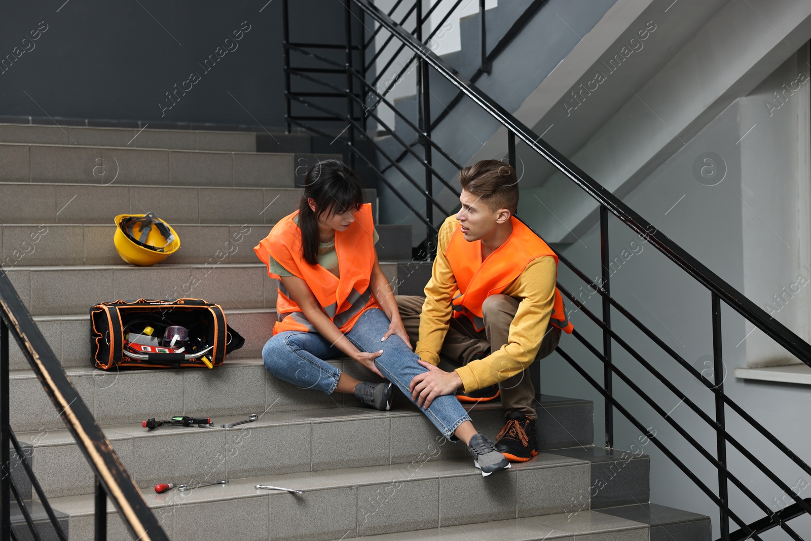 Photo of Accident at work. Man helping his injured colleague on stairs indoors