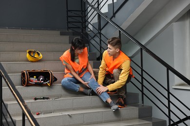 Photo of Accident at work. Man helping his injured colleague on stairs indoors