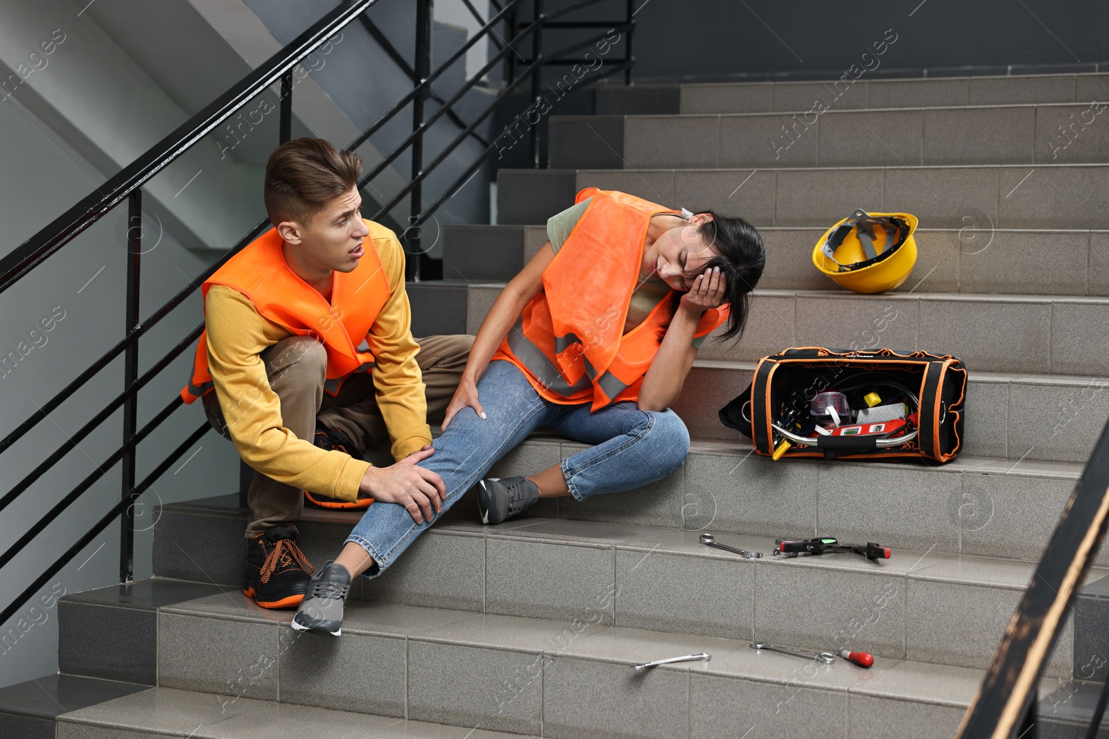 Photo of Accident at work. Man helping his injured colleague on stairs indoors