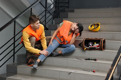 Accident at work. Man helping his injured colleague on stairs indoors