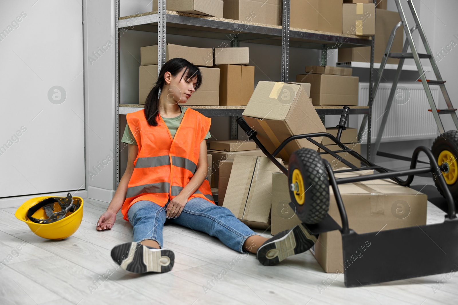 Photo of Accident at work. Unconscious woman and overturned hand truck on floor in warehouse