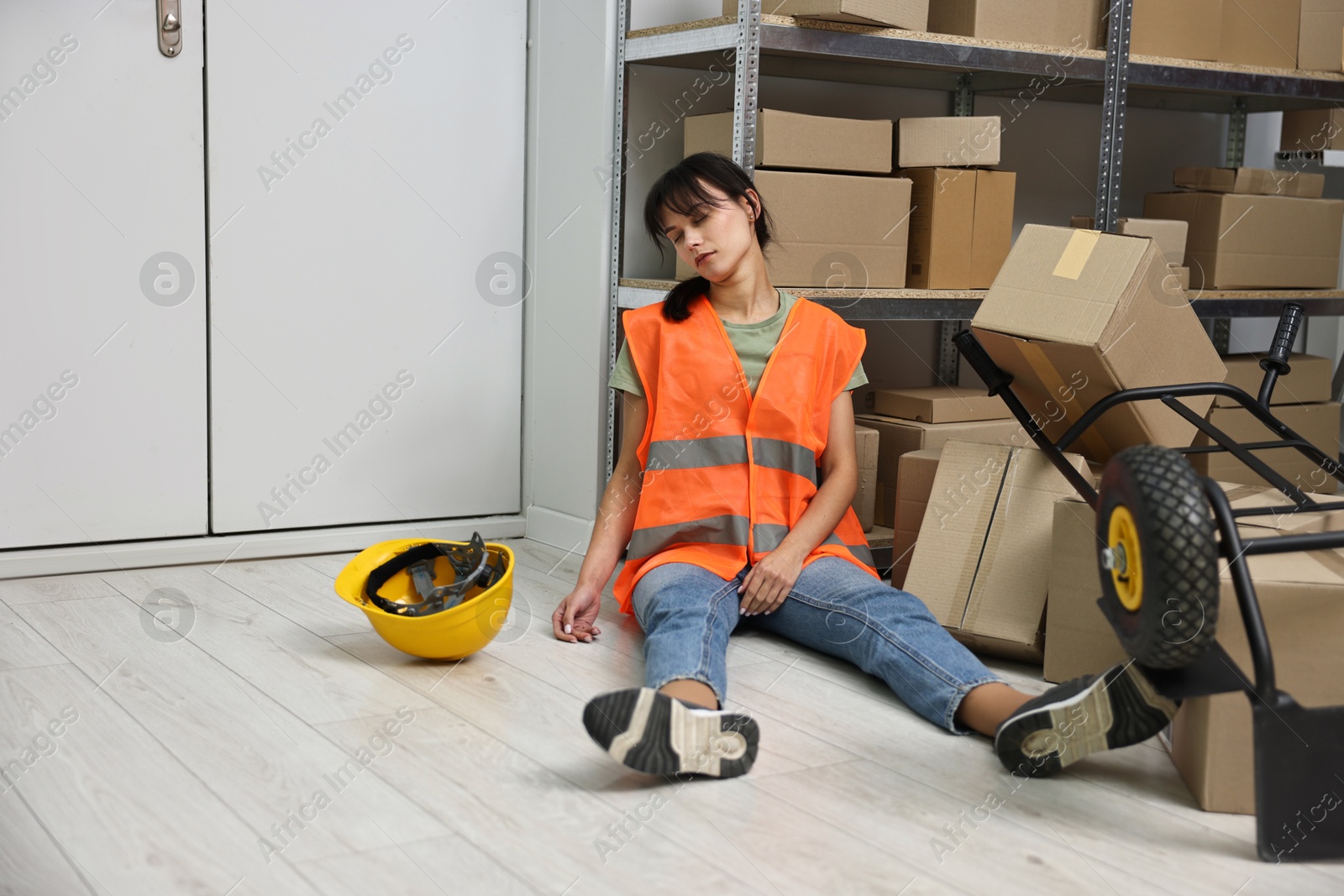 Photo of Accident at work. Unconscious woman and overturned hand truck on floor in warehouse. Space for text