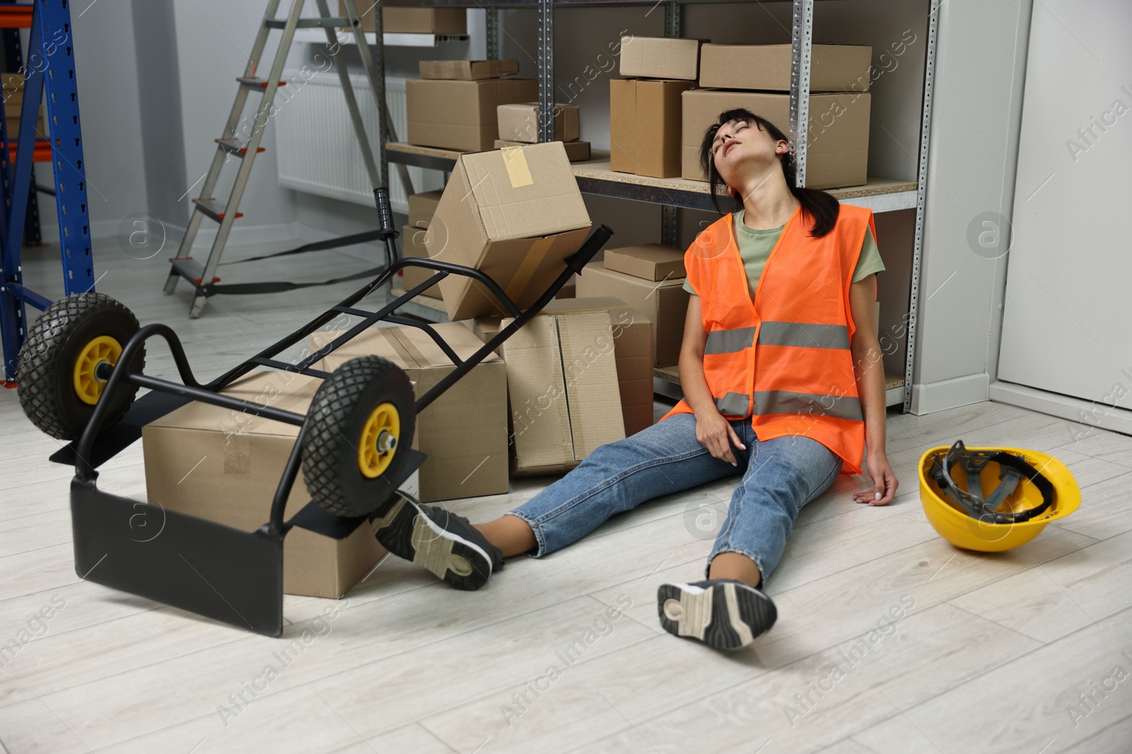 Photo of Accident at work. Unconscious woman and overturned hand truck on floor in warehouse