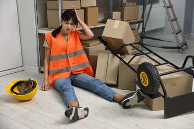 Photo of Accident at work. Injured woman and overturned hand truck on floor in warehouse