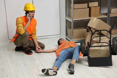 Photo of Accident at work. Man calling ambulance for his unconscious colleague in warehouse