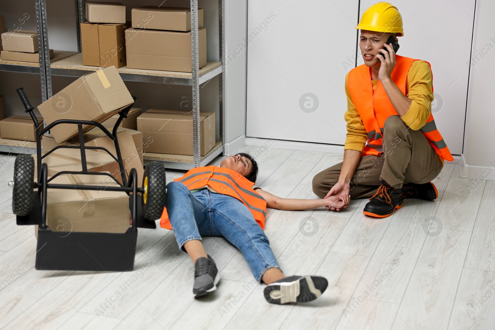 Photo of Accident at work. Man calling ambulance for his unconscious colleague in warehouse