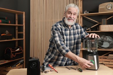 Photo of Relaxing hobby. Senior man repairing blender in workshop