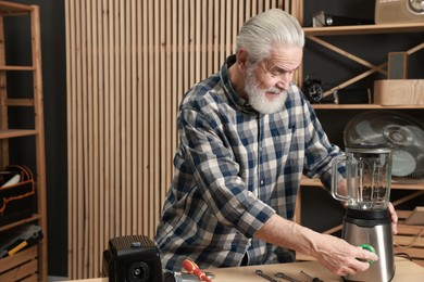 Photo of Relaxing hobby. Senior man repairing blender in workshop