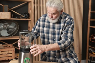 Photo of Relaxing hobby. Senior man repairing blender in workshop