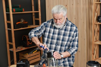 Photo of Relaxing hobby. Senior man repairing blender with pliers in workshop