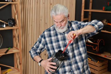 Photo of Relaxing hobby. Senior man repairing blender with screwdriver in workshop